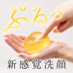 こんにゃく石けんぷるりの画像。手のひらに乗せた黄色いこんにゃく石けんを、指先で押すことでやわらかさを伝えている写真。 ぷるっといつ擬音の文字と新感覚洗顔の文字の装飾がある。